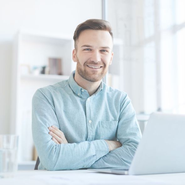 Portrait of handsome entrepreneur smiling happily at camera while posing at workplace in office, copy space